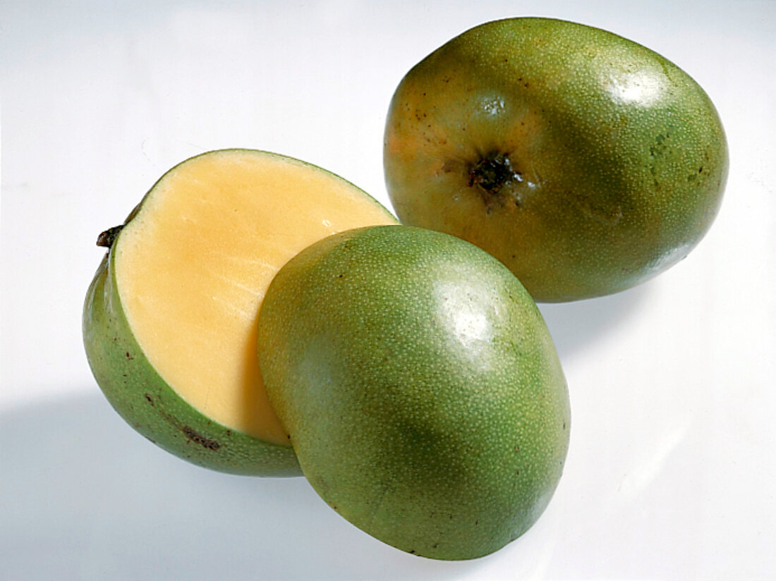 Whole and halved green mangoes on white background
