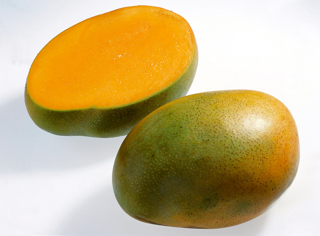 Whole and halved yellow mango on white background