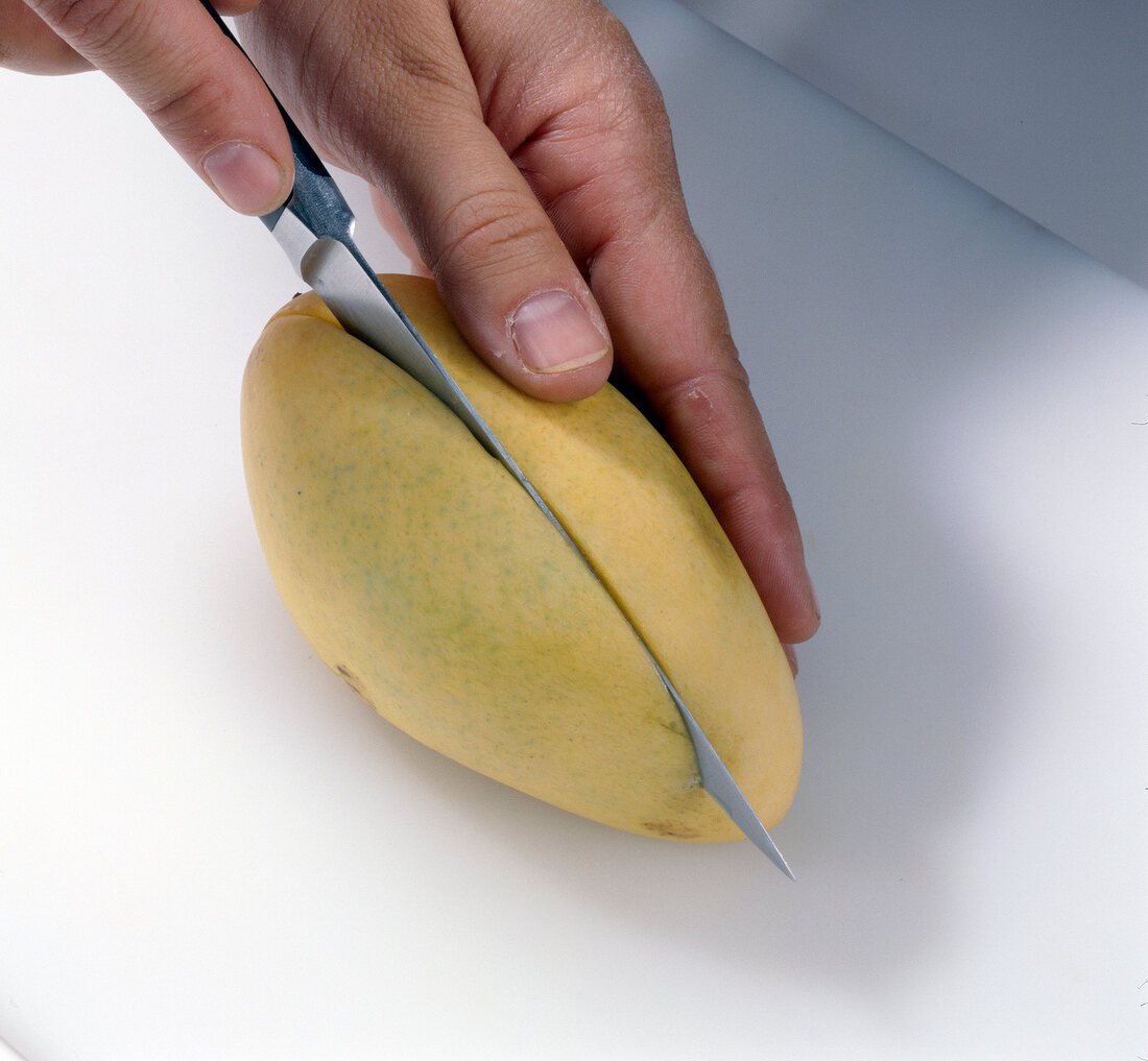 Mango being cut into half with knife, step 1