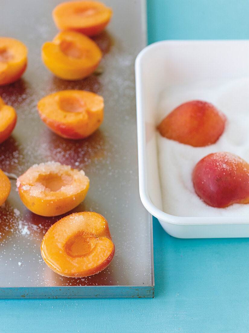 gezuckerte Aprikosen auf Backblech, Schale mit Zucker und Aprikosen
