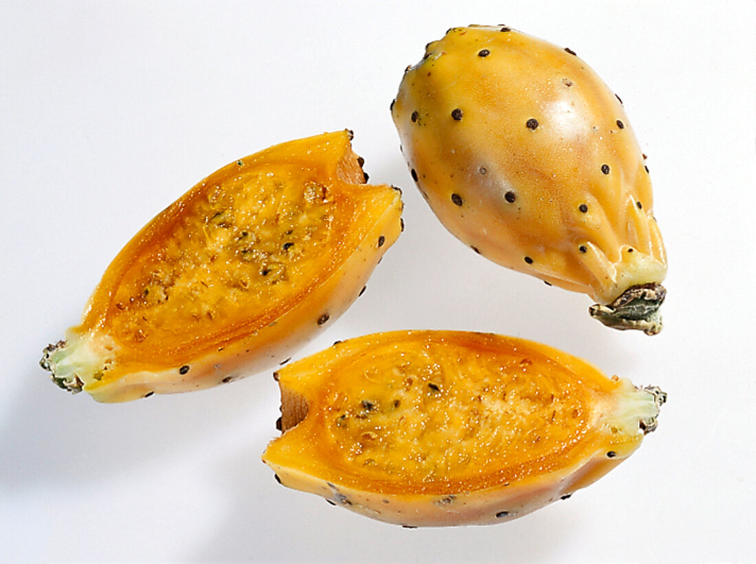 Whole and halved orange and yellow oval shaped cactus figs on white background