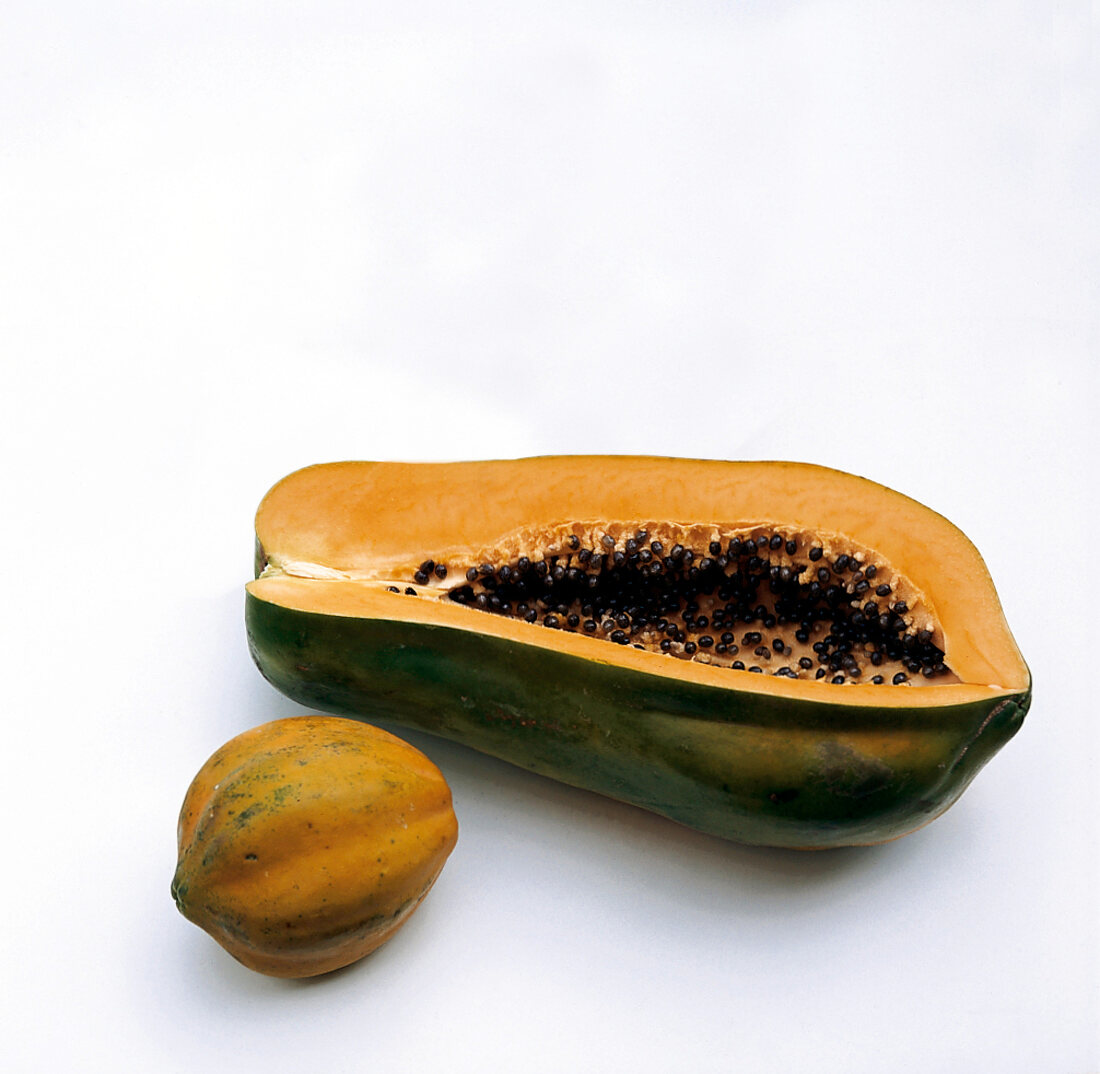 Halved large papaya and whole small papaya on white background