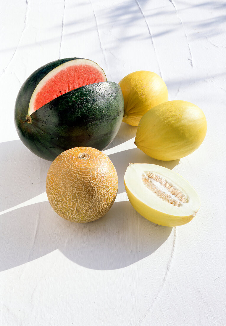 Watermelon, honeydew melon and whole and halved galia melon on white surface