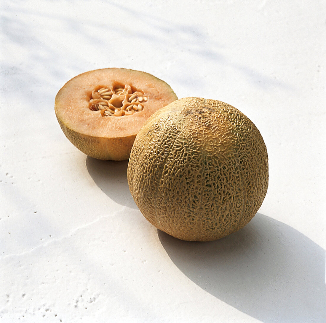Whole and half ripe cantaloupe melon on white surface