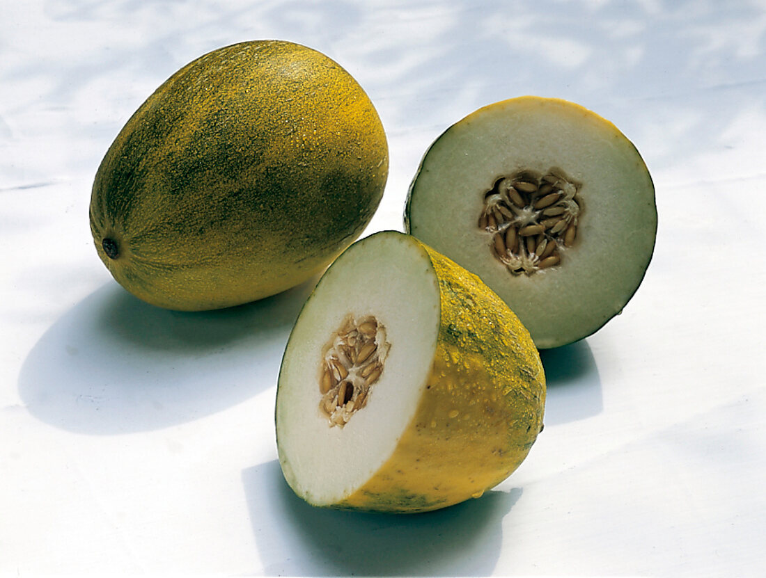 Whole and halved green honeydew melons on white surface