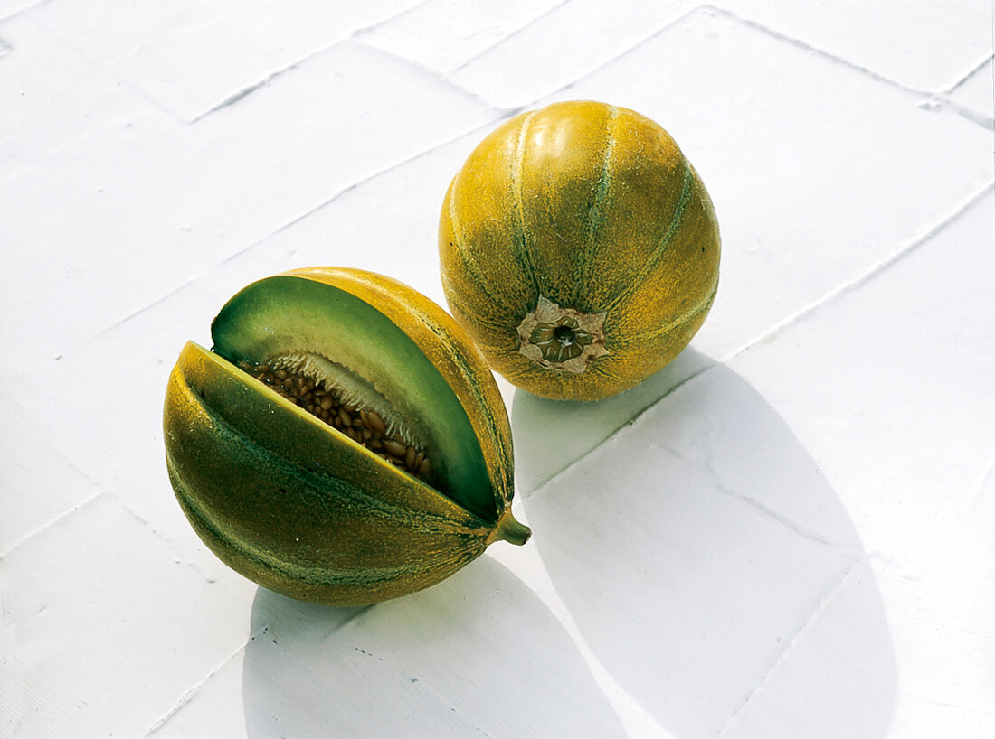 Whole and halved yellow and green ogen melon on white surface