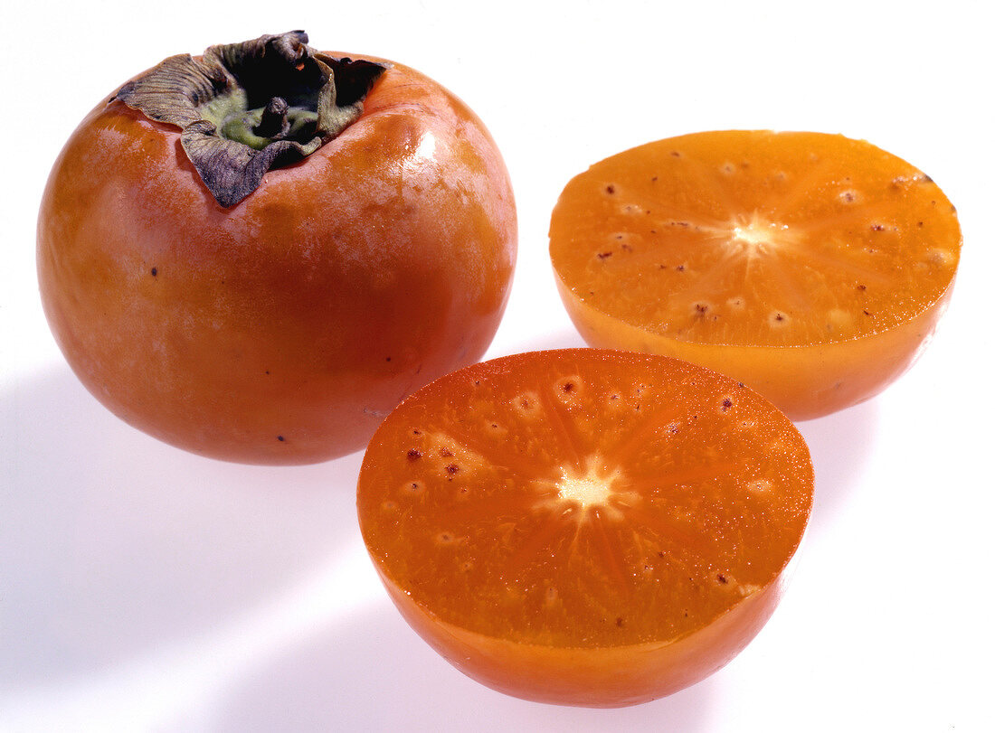 Whole and halved persimmon fruit on white background