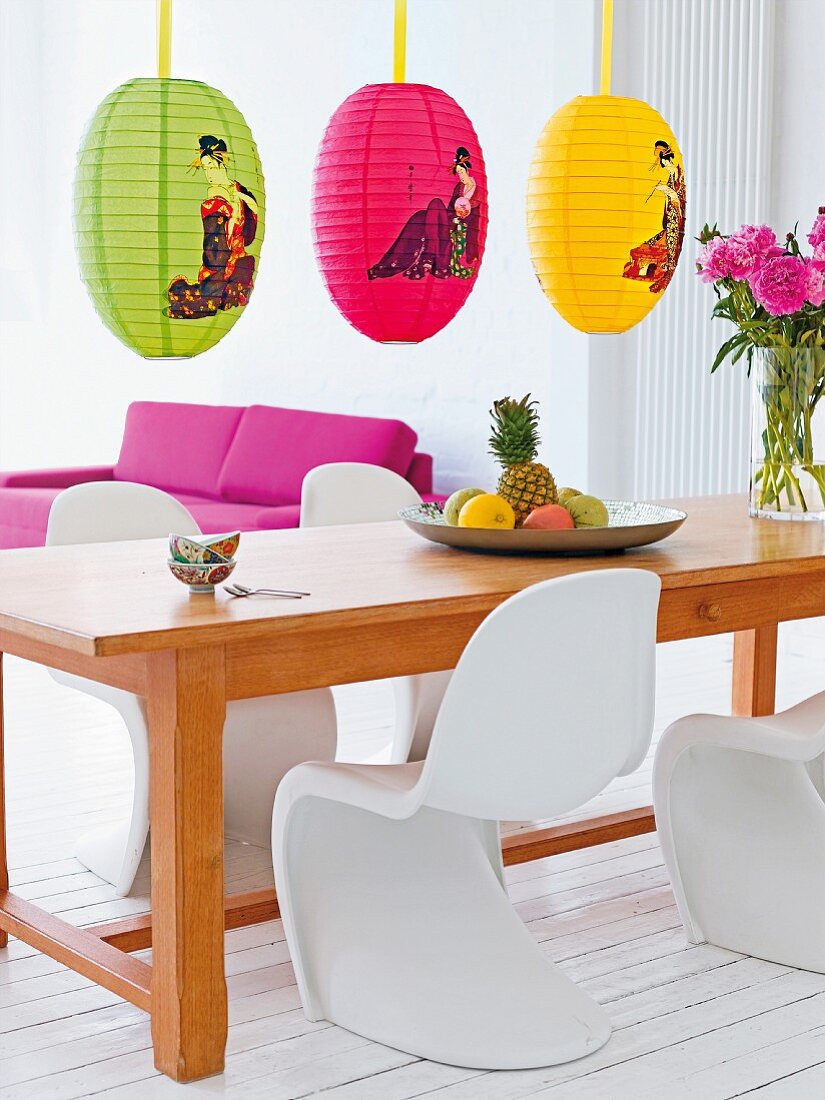 A long wooden dining table with white panton chairs and colourful, oriental-patterened paper lanterns