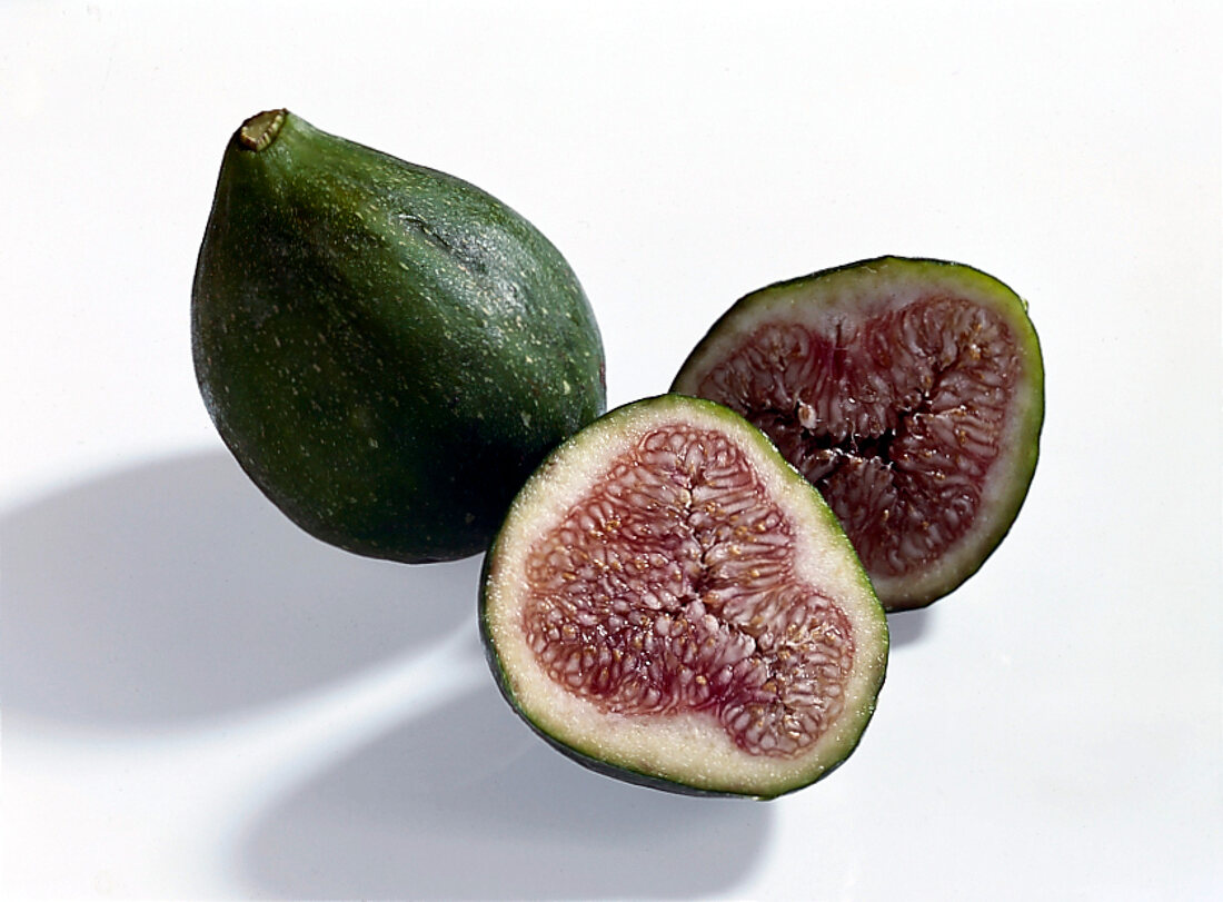 Halved and whole green figs on white background