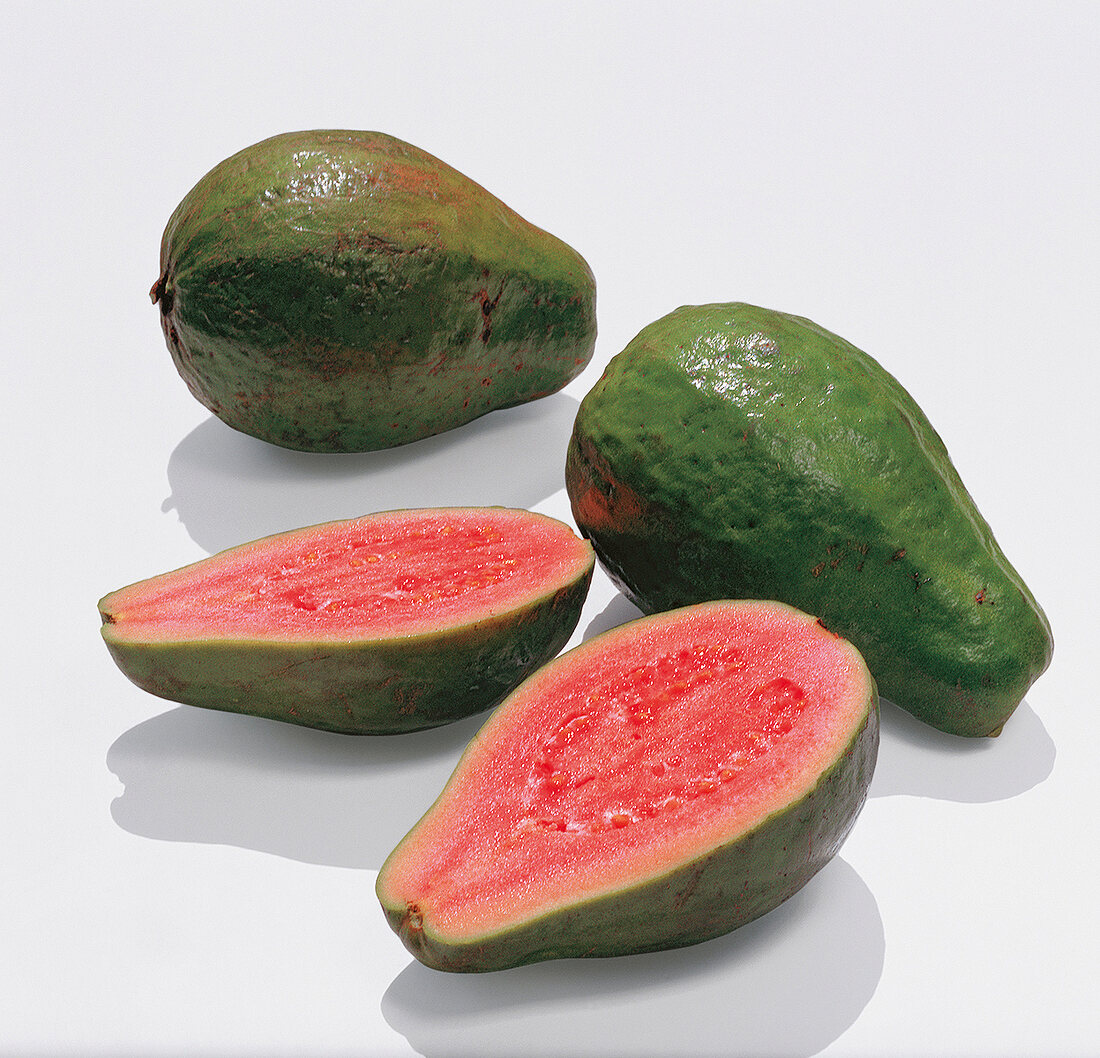 Halved and whole green guavas with pink flesh on white background