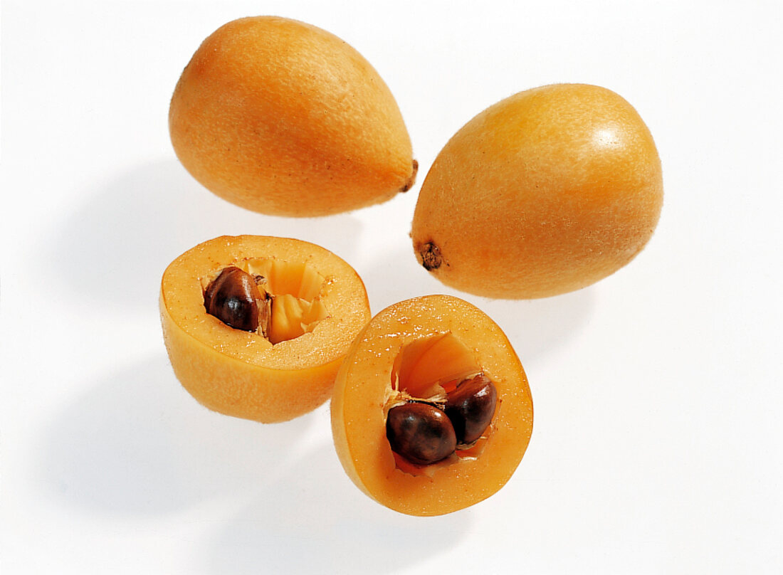 Halved and whole loquat on white background