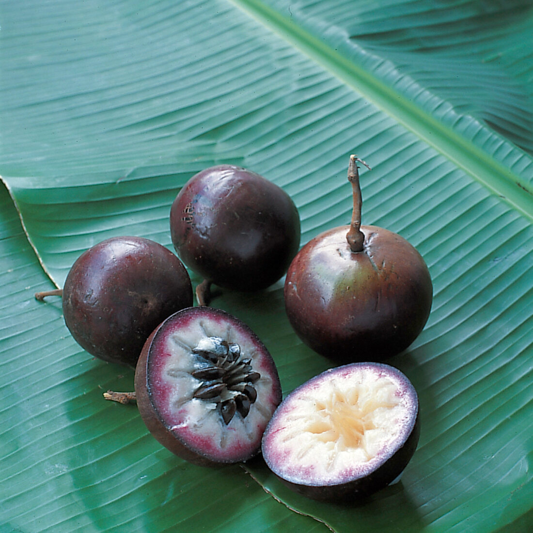 Whole and halved star apples on banana leaf