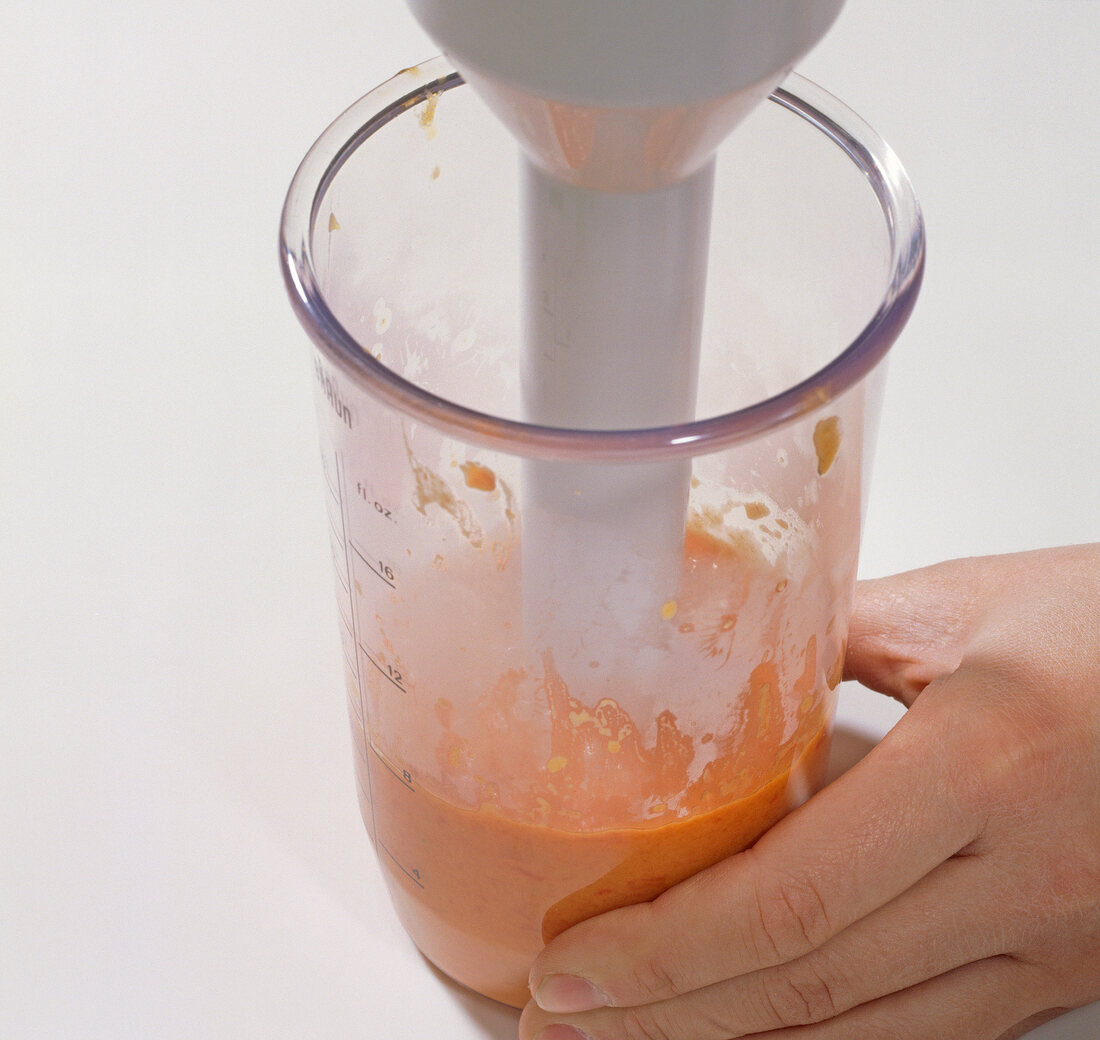 Diced peppers being pureed in glass jar with hand blender, step 2