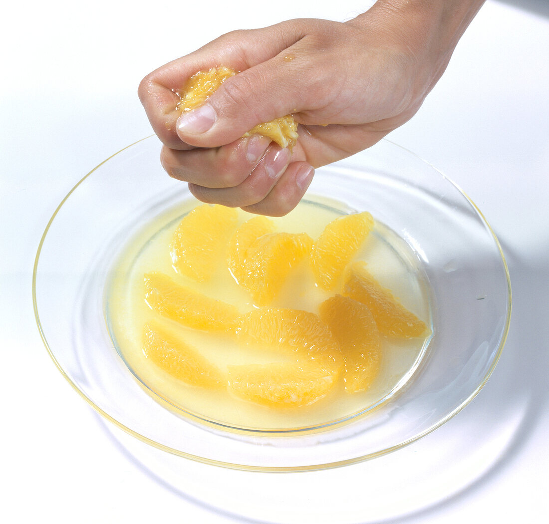 Close-up of hand squeezing orange pulp for juice on plate