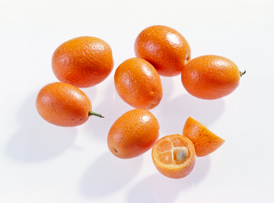 Whole and halved kumquats on white background