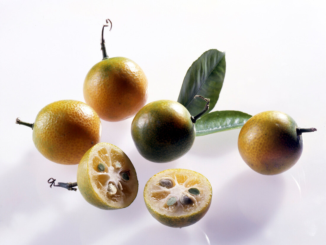 Whole and halved green kumquats on white background