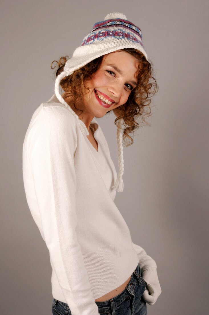 Portrait of beautiful woman with curly hair wearing white sweater and cap, smiling widely