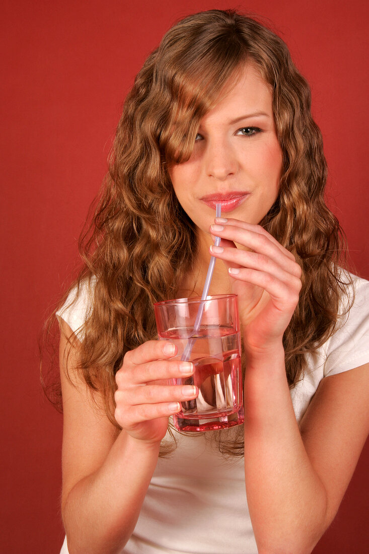 Pretty woman holding glass of water and sipping it through straw, smiling