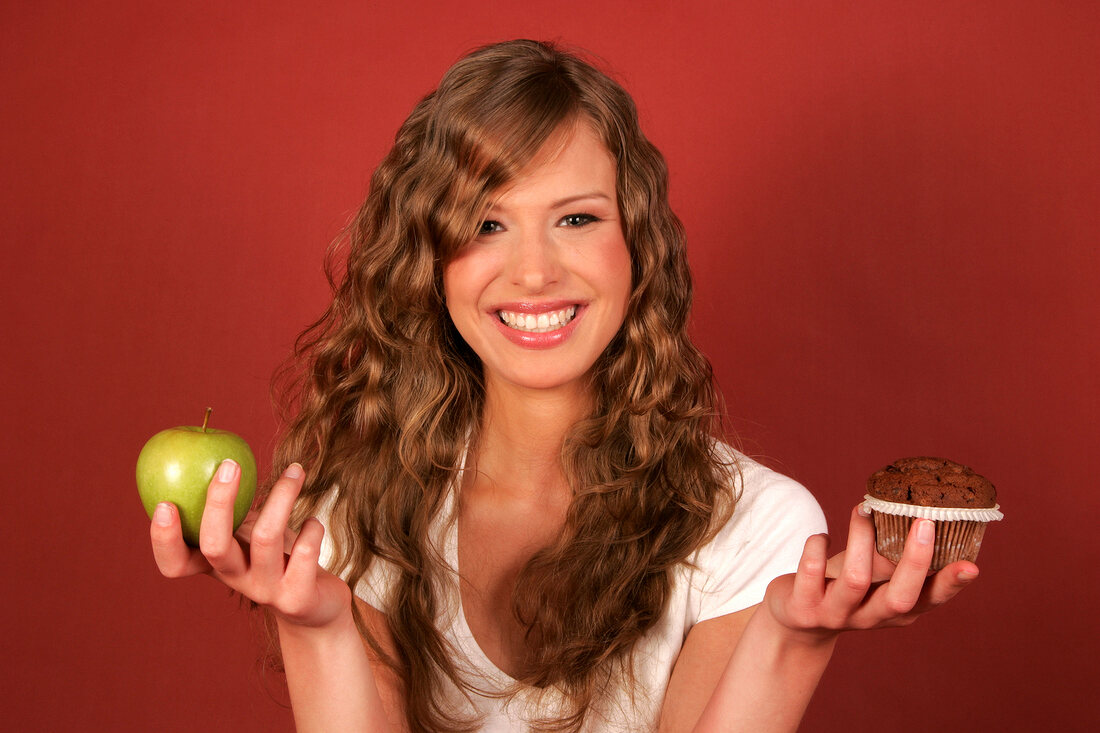 Woman holding apple and muffin in hands, smiling
