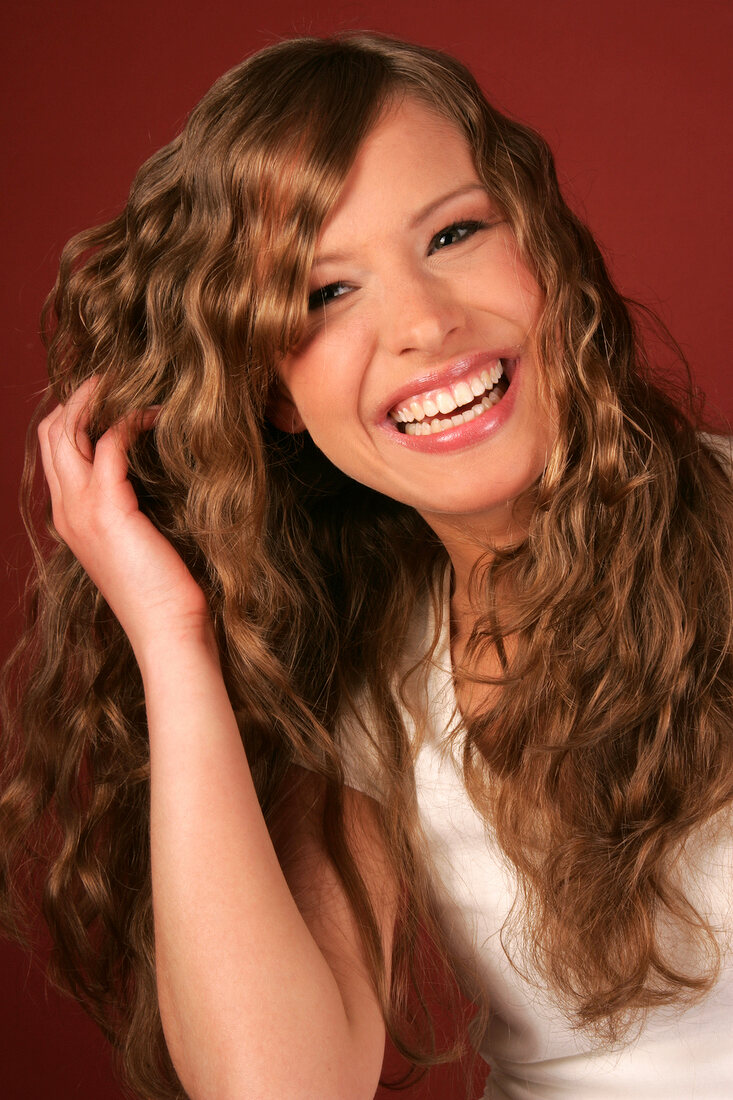 Portrait of beautiful woman with long curly hair in white top smiling with hand in hair