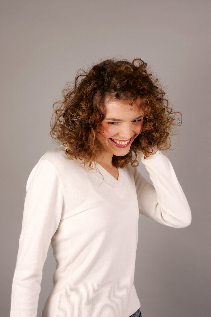 Beautiful woman with curly hair wearing white sweater standing with hand in hair, smiling