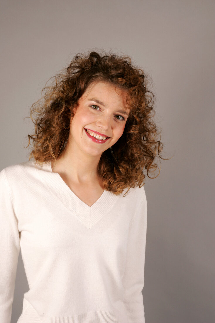 Portrait of happy young woman with curly hair wearing white sweater, smiling