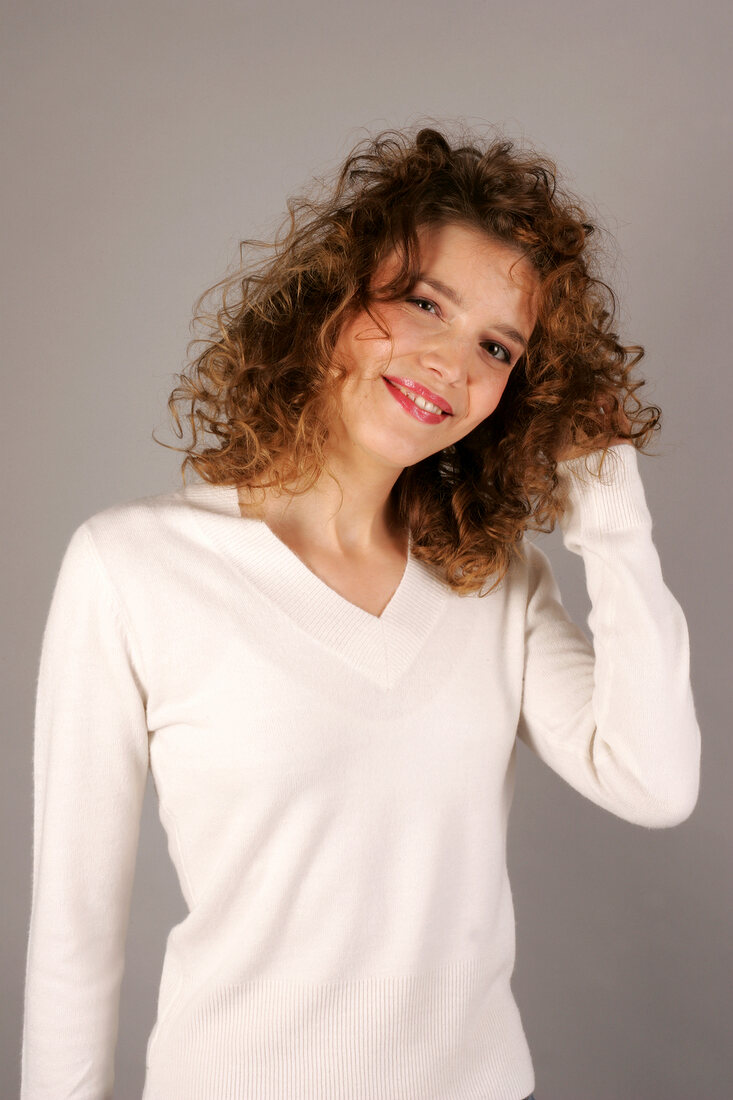 Beautiful woman with curly hair wearing white sweater standing with hand in hair, smiling