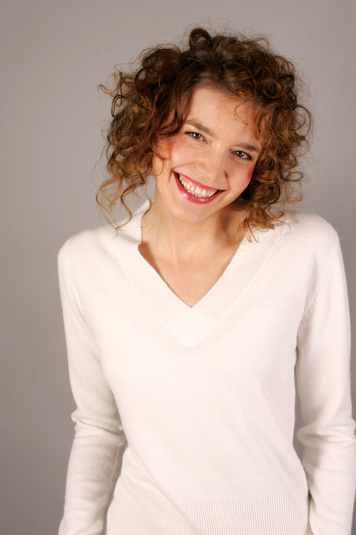 Portrait of beautiful woman with curly hair wearing white sweater, smiling widely
