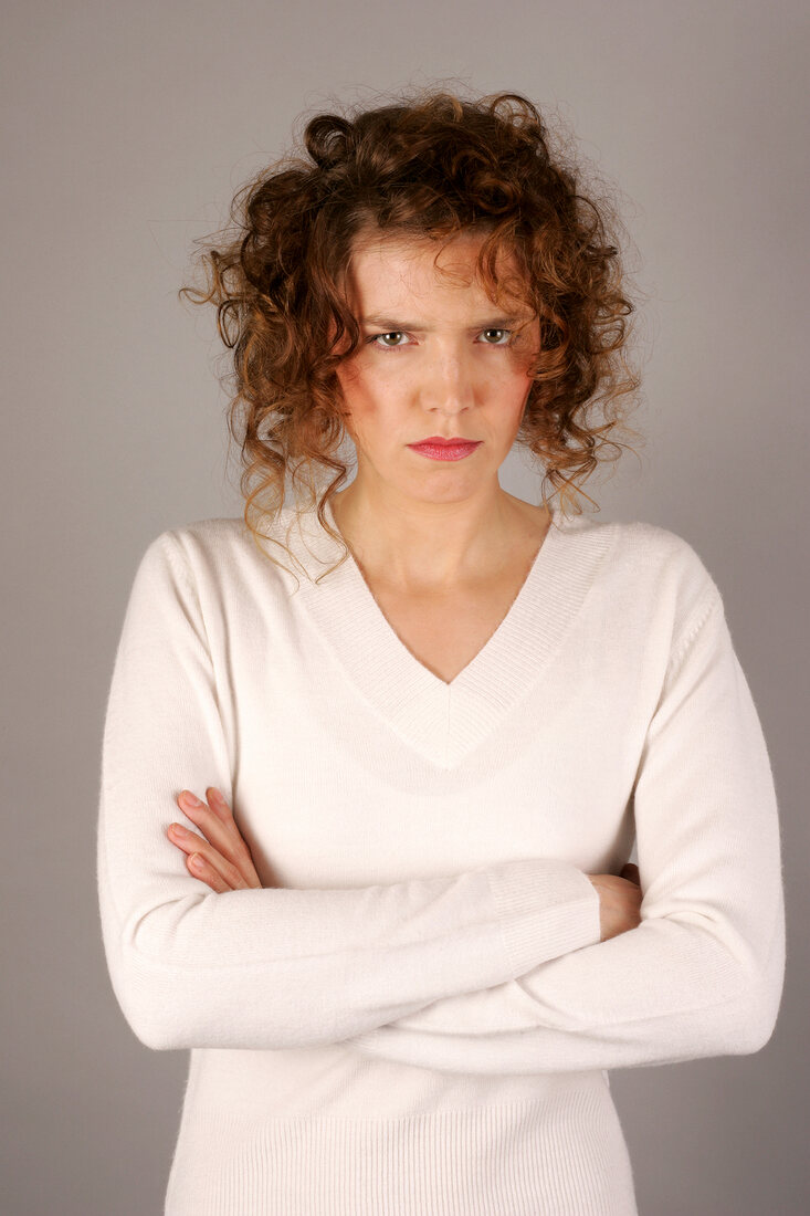 Portrait of angry woman with curly hair wearing white sweater standing with arms crossed