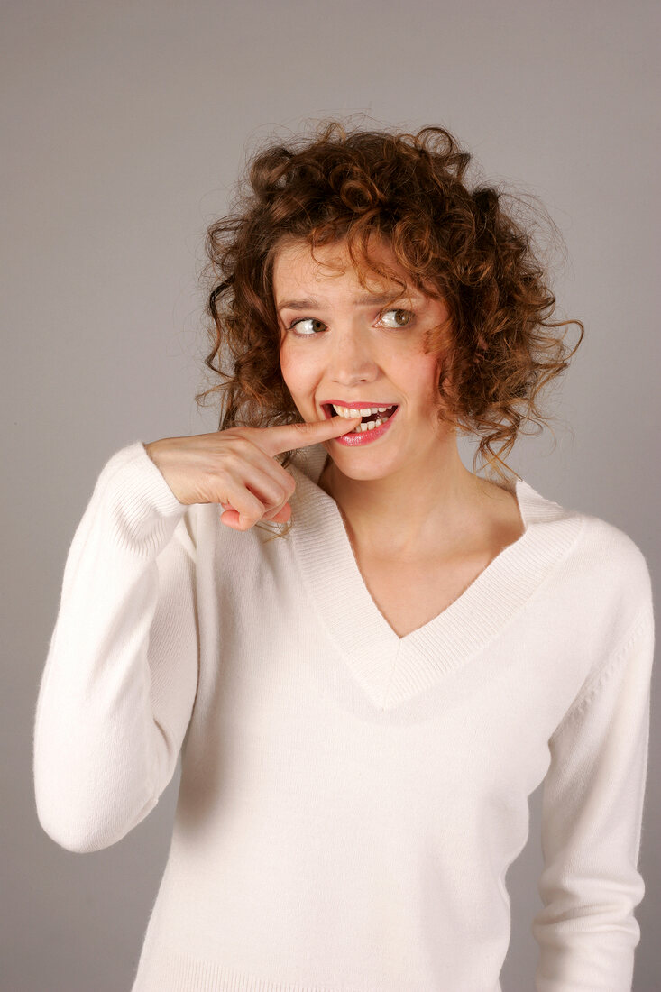 Worried young woman with curly hair, looking sideways and biting her finger