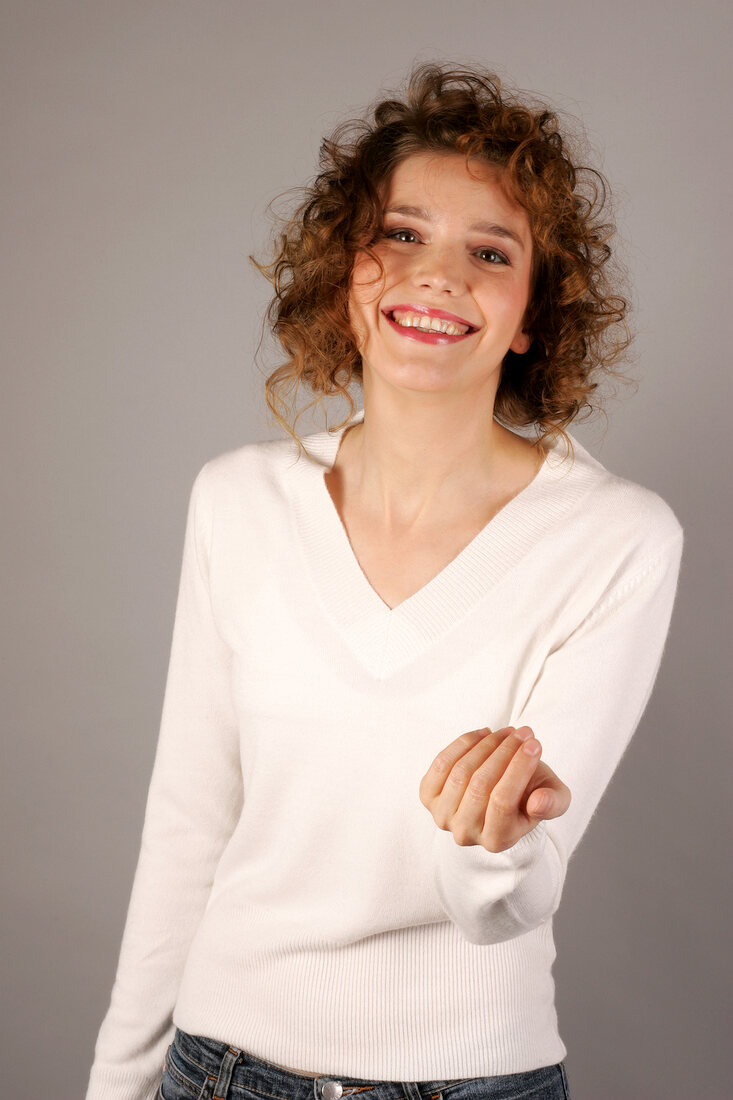 Cheerful young woman with curly hair wearing white sweater, smiling with hand put forward