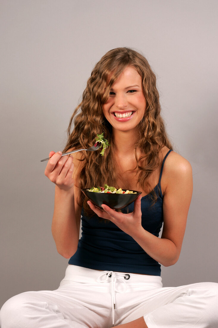 Sandra sitzt Schneidersitz hat Schüssel mit Salat in der Hand