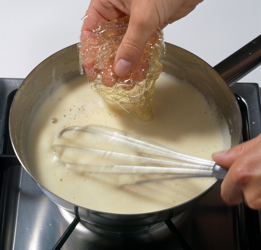 Close-up of hand adding gelatine in pot with passion fruit cream