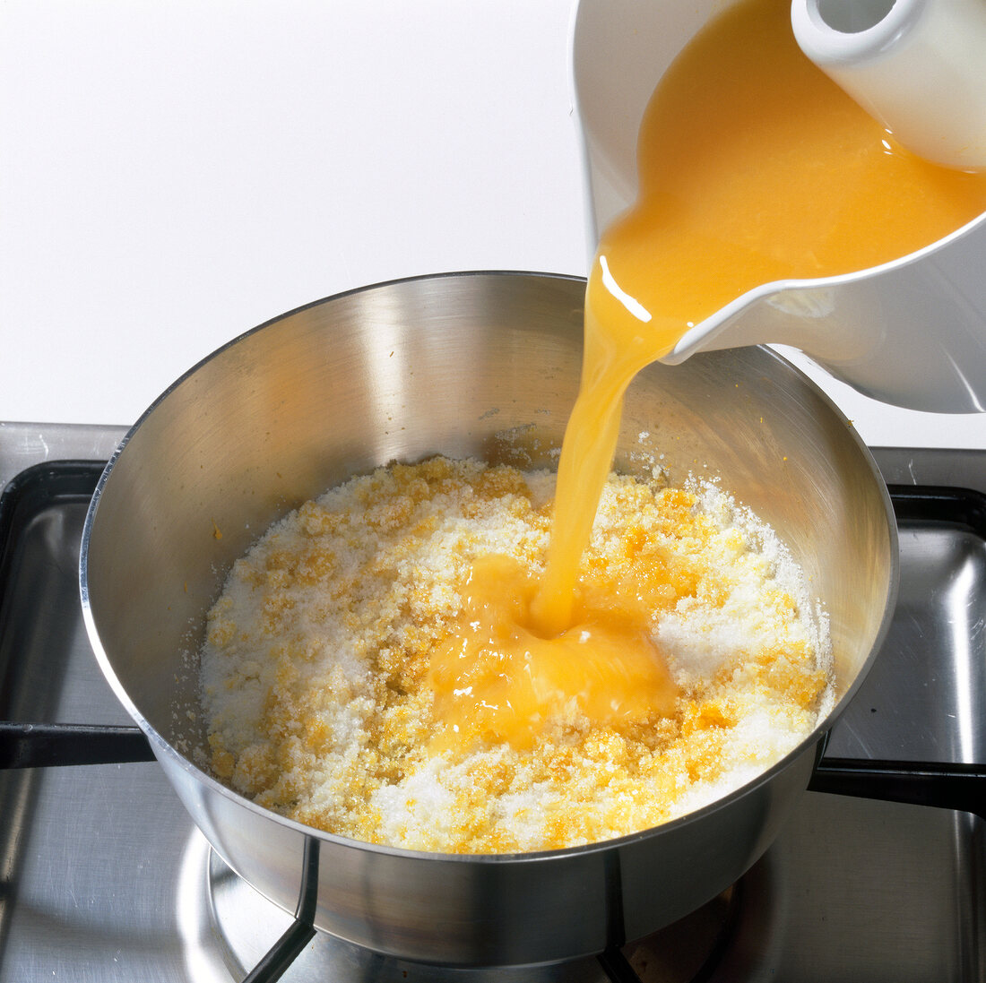 Orange juice being poured in mixture of sugar and orange zest in pot