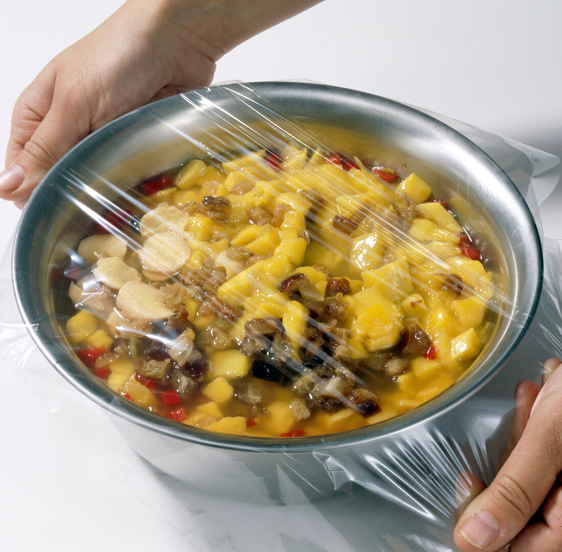 Pot with mango, raisins and dates being covered with cellophane