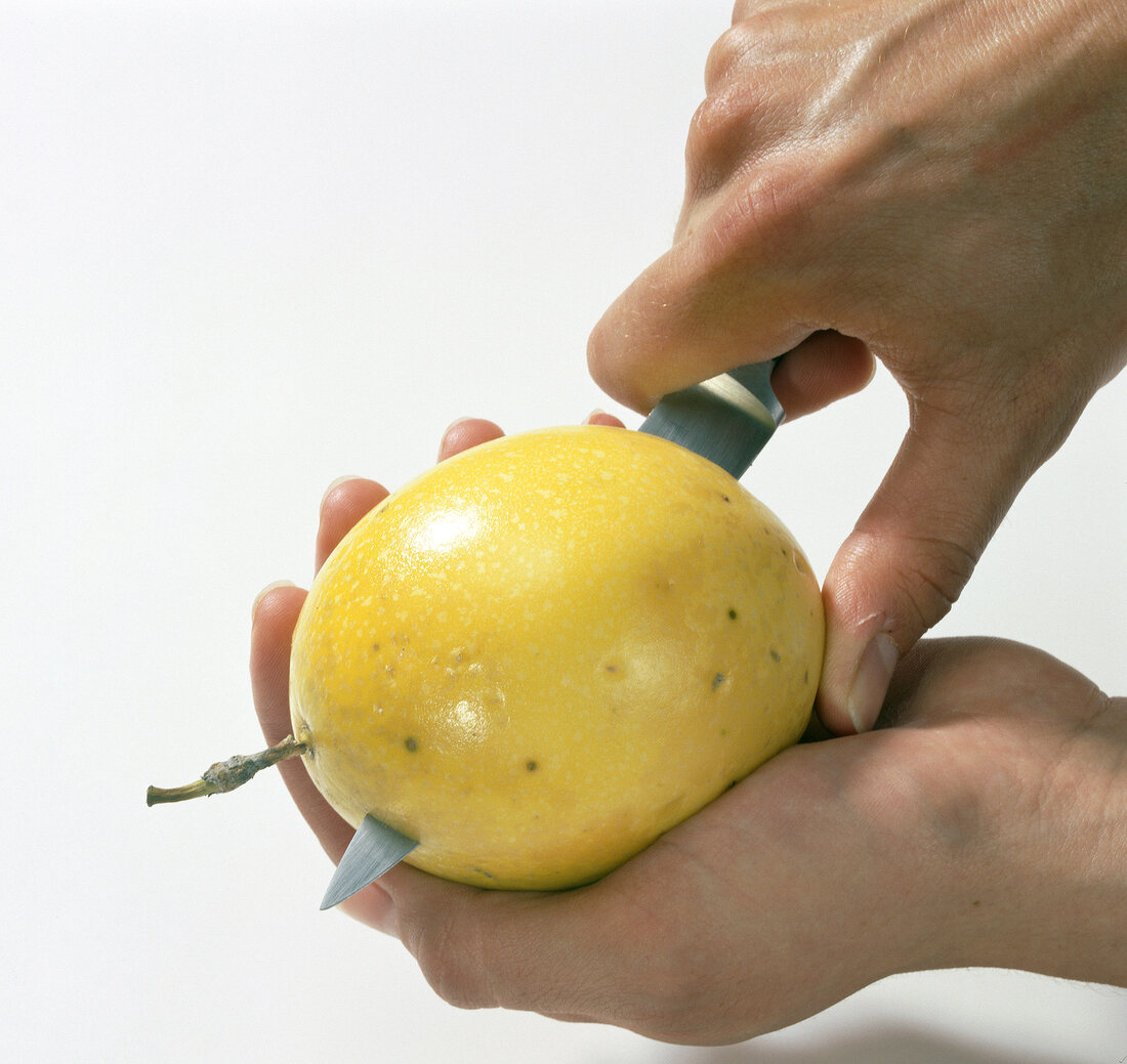 Close-up of hand cutting passion fruit on white background