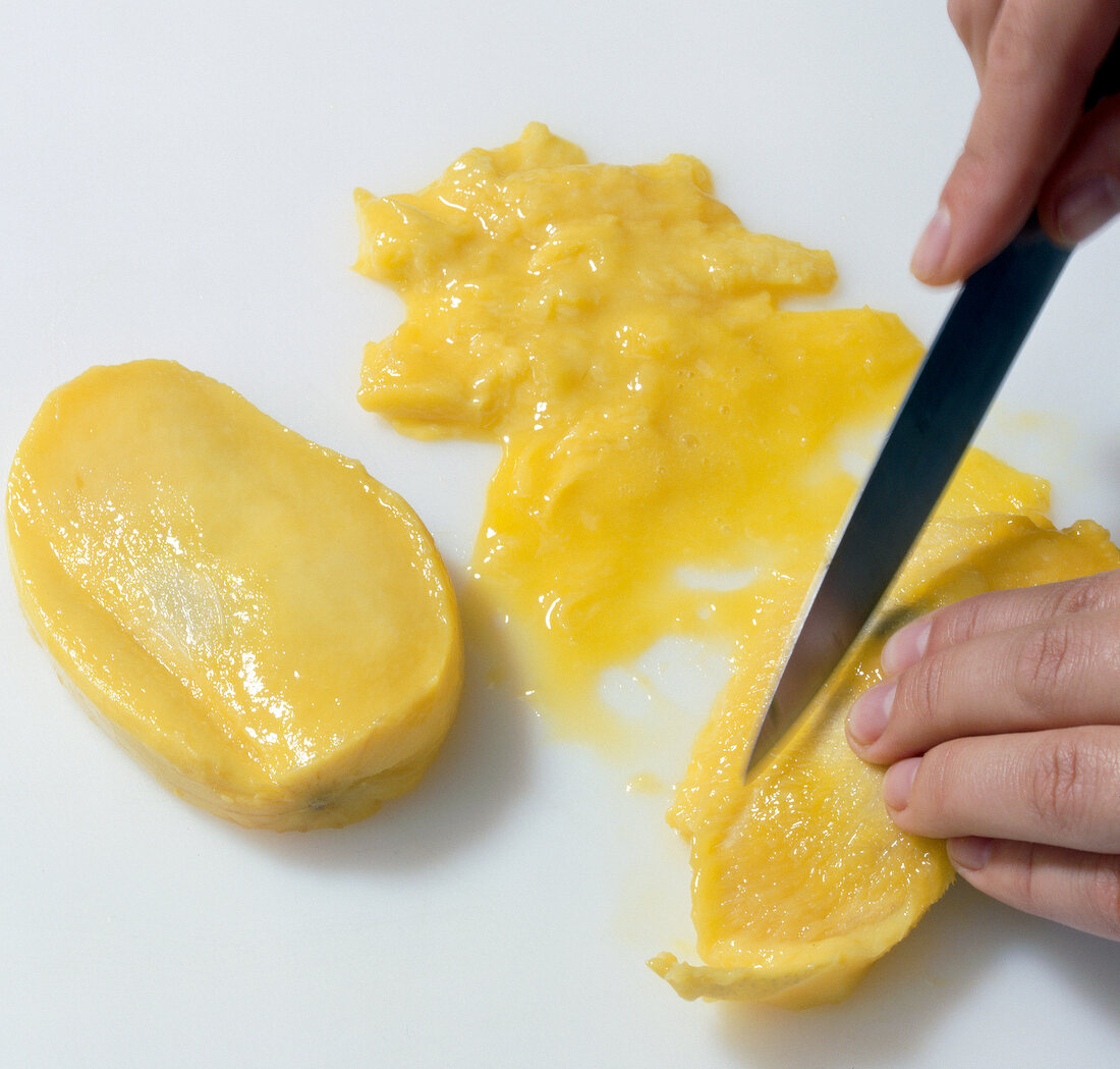 Close-up of hand cutting mango fruit flesh from core