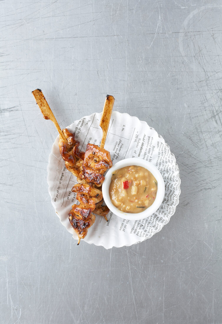 Satay skewers with peanut sauce on paper plate