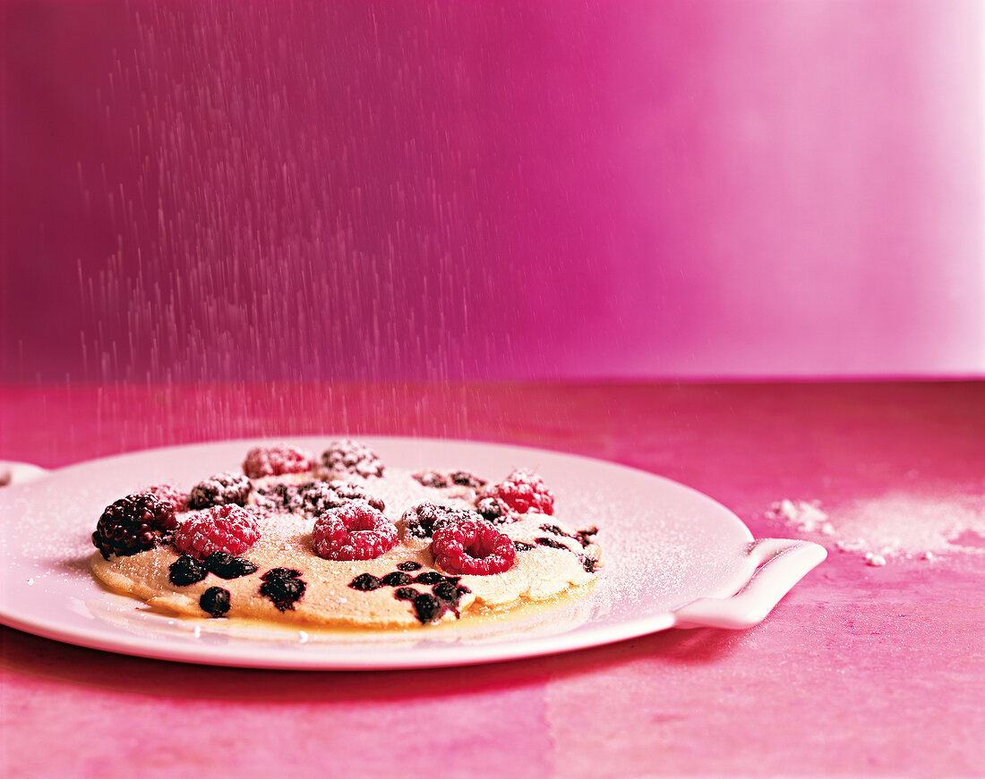 Pancake topped with berries and powdered sugar on tray