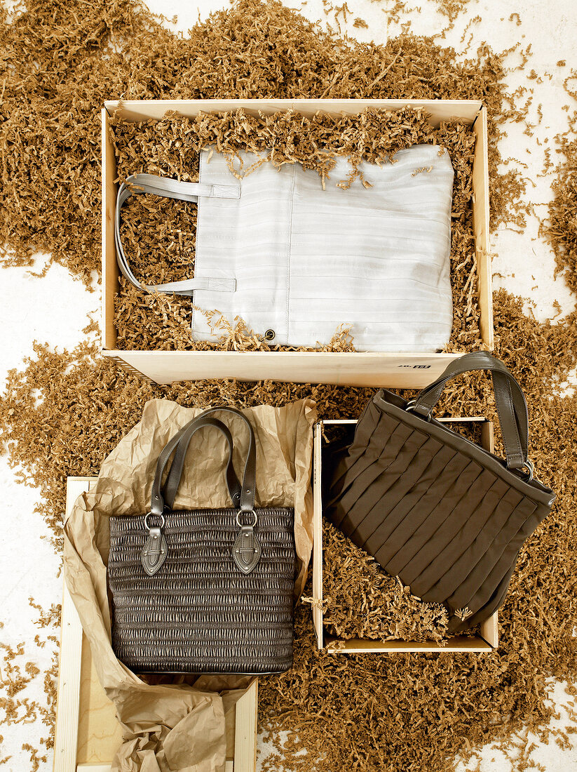 3 Handtaschen in Braun und Weiß liegen in Holzspänen