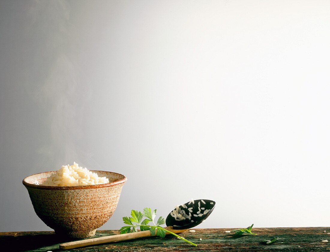 Dampfender gekochter Reis in Schale, Holzlöffel und Petersilie
