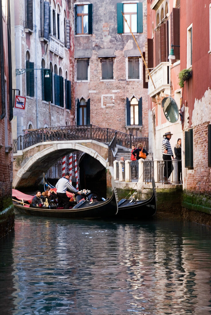 Tourists enjoying gondola ride in narrow canal, Venice, Italy