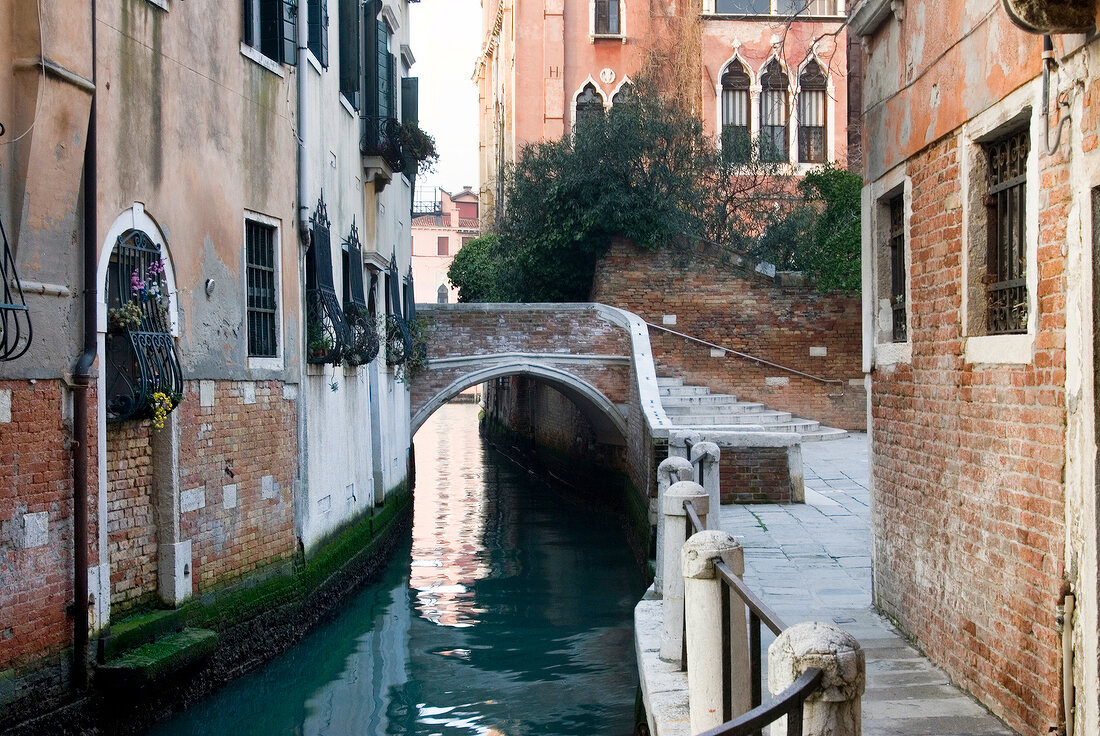 View of narrow canal, railing, houses and bridge in Campiello Barbaro, Venice, Italy
