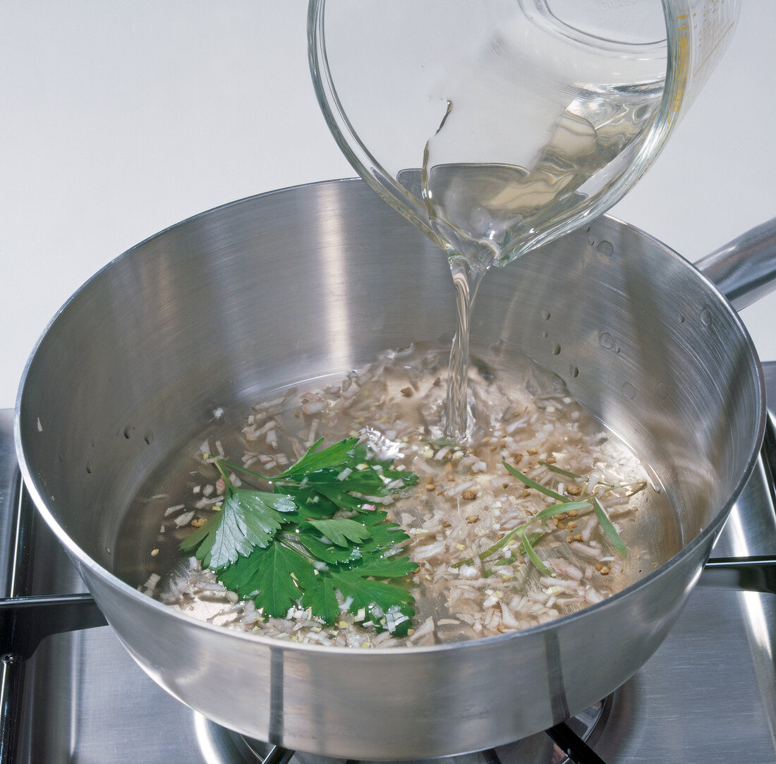 Close-up of white wine being poured on other ingredients in pan, step 2
