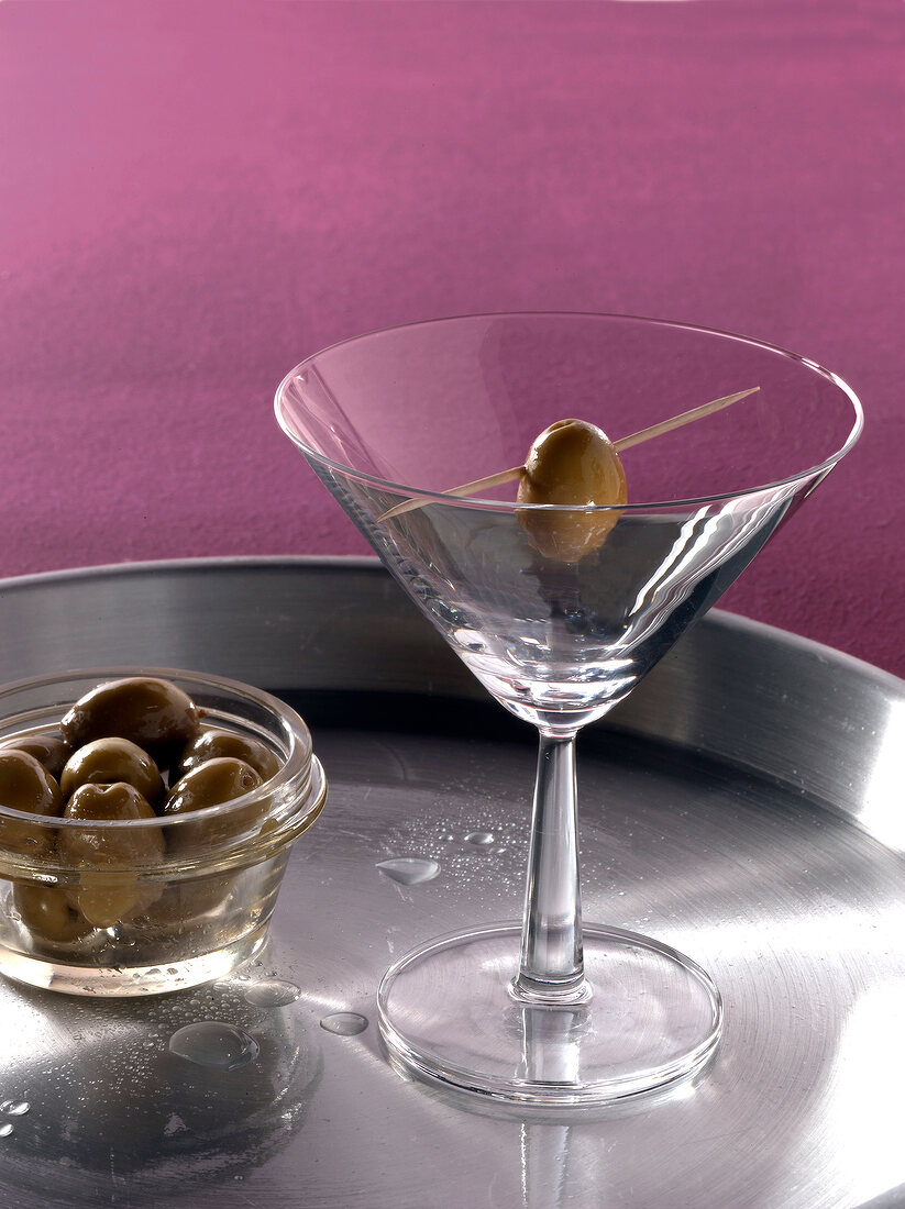 Cocktail glass with skewered olive on tray