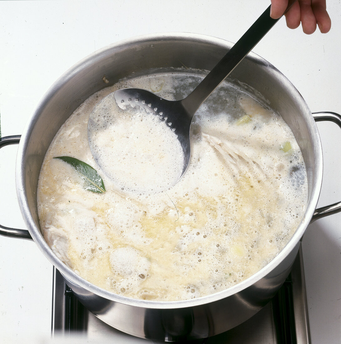 Foam being removed from boiling mixture in pot for preparation of fish stock, strep 7