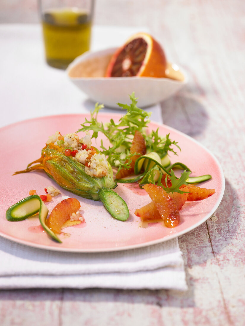 Zucchini blossom with scampi tartare, vegetables couscous and blood oranges on plate