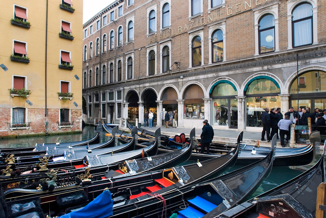 Mehrere Gondeln in Reihe vor Fassade mit Arkaden, Venedig