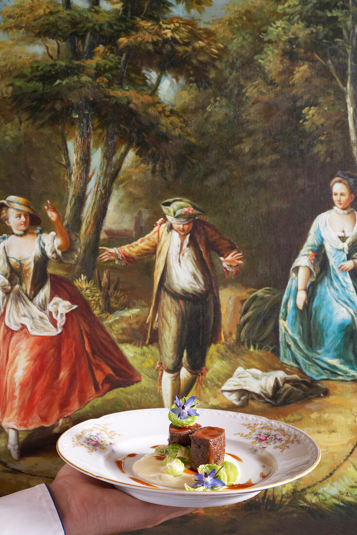Rehkitz mit Kastanien und Rosenkohl auf Teller, Gemälde im Hintergrund
