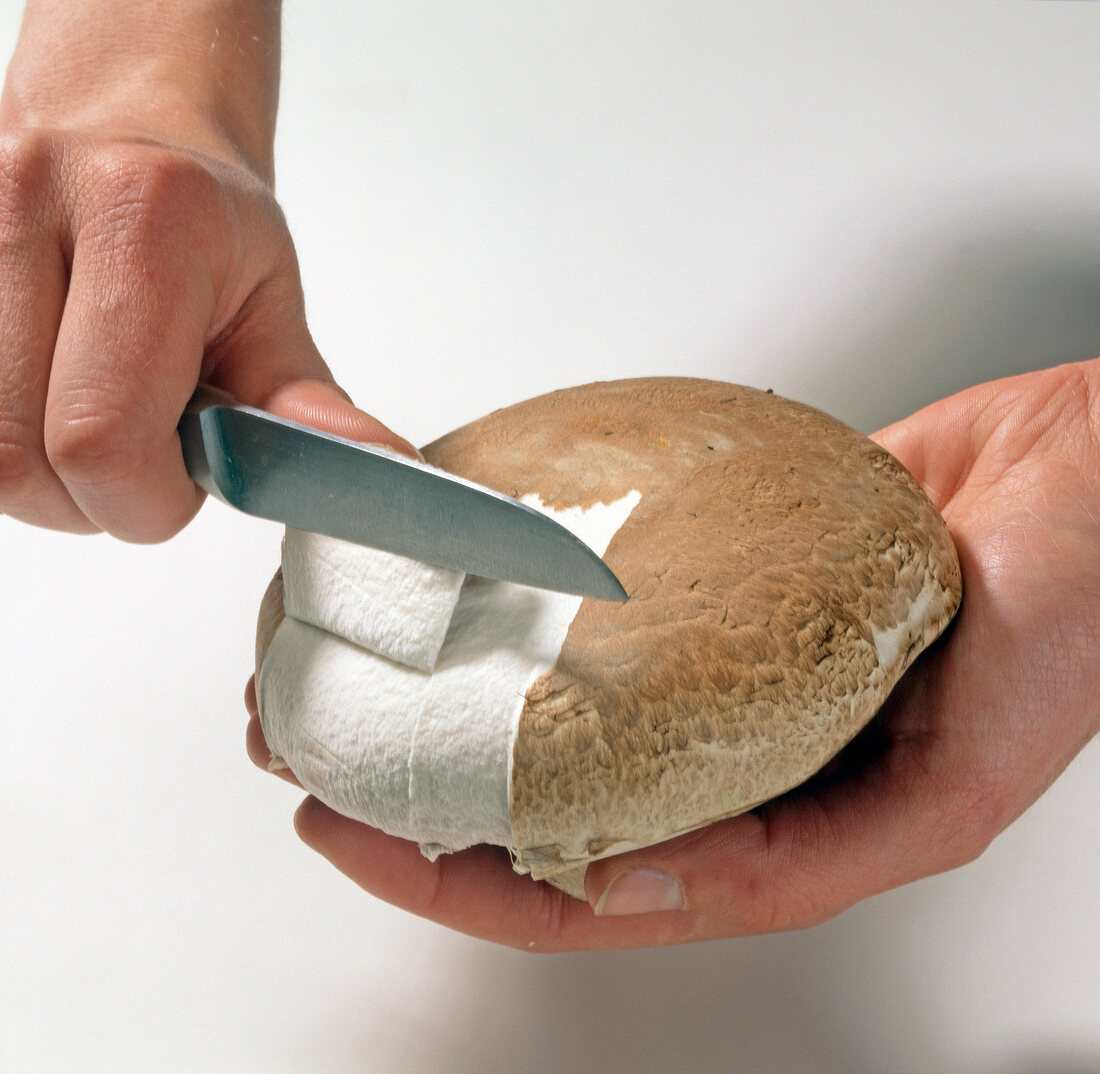 Close-up of hand peeling portobello mushroom with knife, step 1
